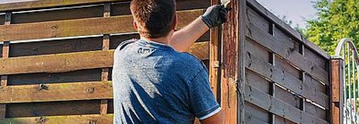 Person streicht einen Holzzaun mit einem Pinsel.